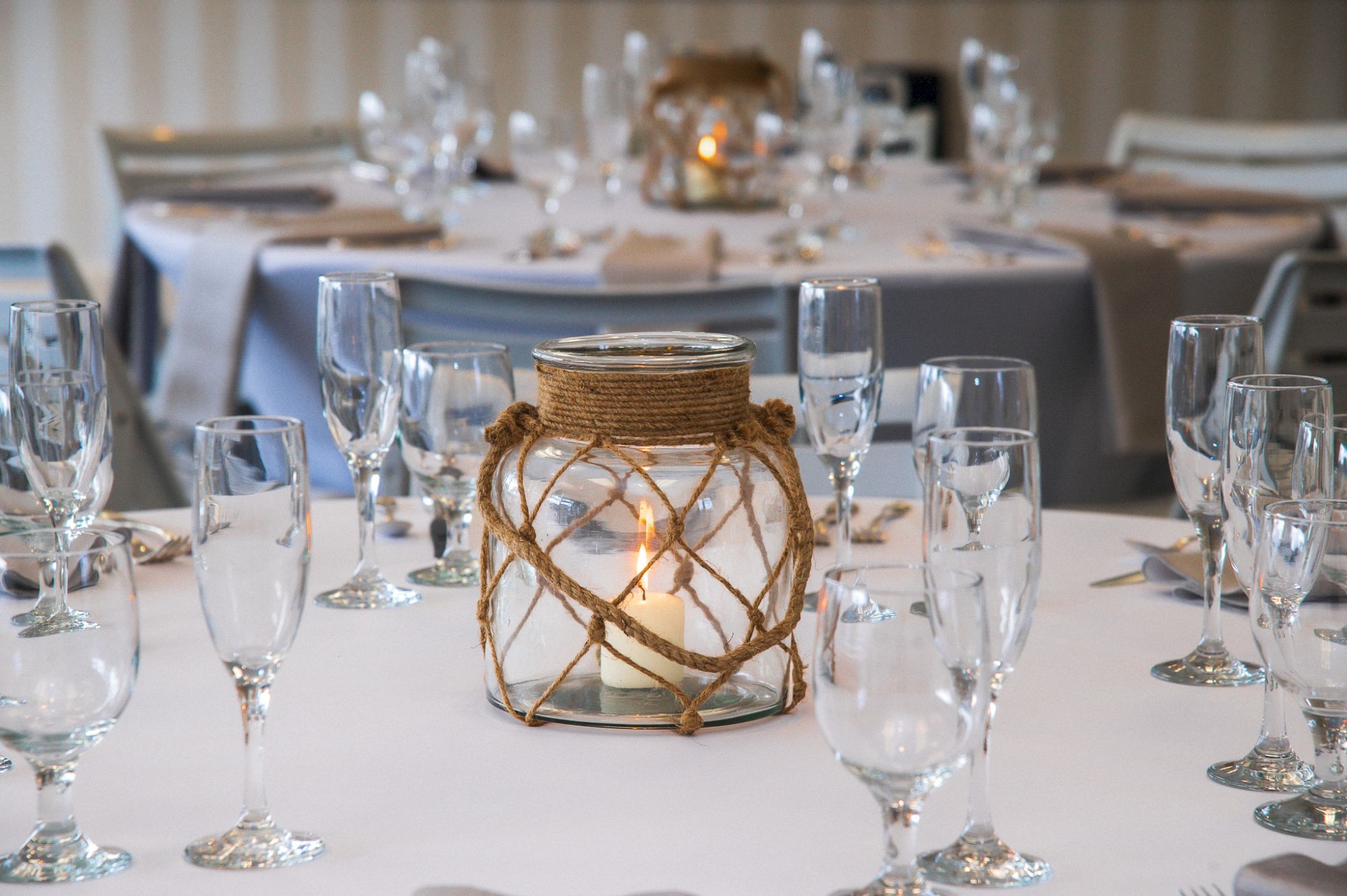 A decorated table set for an event, featuring a centerpiece with a candle in a glass jar and surrounded by empty champagne glasses.