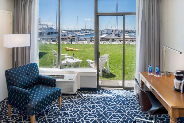 A modern hotel room with a polka-dot chair, desk, and seaside view, showing boats and patio chairs outside.