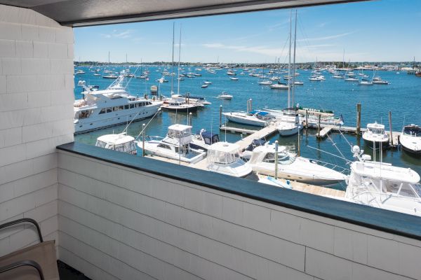 View of a marina with numerous boats docked in the clear blue water, seen from a window or balcony with white paneling.