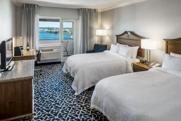 The image shows a hotel room with two double beds, a TV, a desk, and a window view of a marina. The decor is modern and elegant.