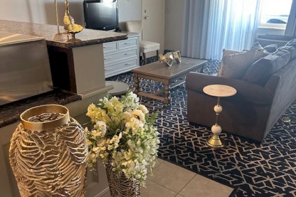 A living room with a sofa, TV, decorative vases with flowers, and a patterned rug. The space has soft lighting and elegant decor.