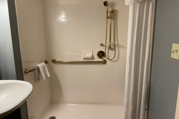 The image shows a shower area with grab bars, a handheld showerhead, a curtain, and a towel rack, suggesting an accessible design.