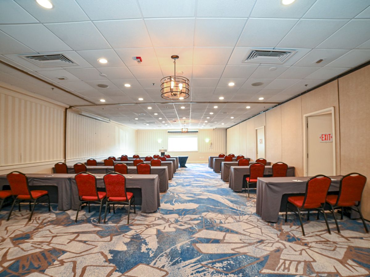 This image shows a conference room setup with rows of tables and chairs, a projector screen at the front, and patterned carpet on the floor.