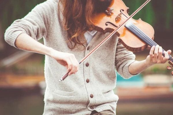 A person is playing a violin outdoors, wearing a gray cardigan.