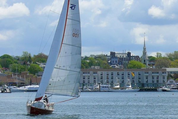 A sailboat on the water with buildings and a church in the background under a partly cloudy sky.