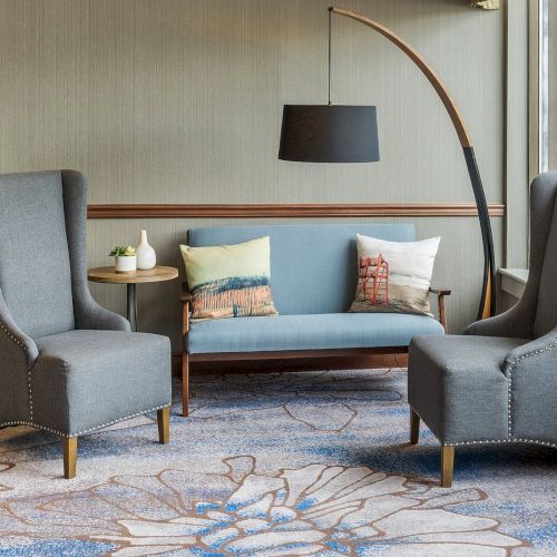 A stylish living room with two gray armchairs, a sofa, and a curved floor lamp, featuring a decorative blue-patterned rug on the floor.