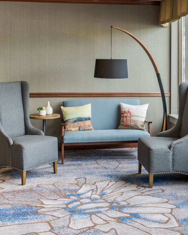 A stylish living room with two gray armchairs, a sofa, and a curved floor lamp, featuring a decorative blue-patterned rug on the floor.