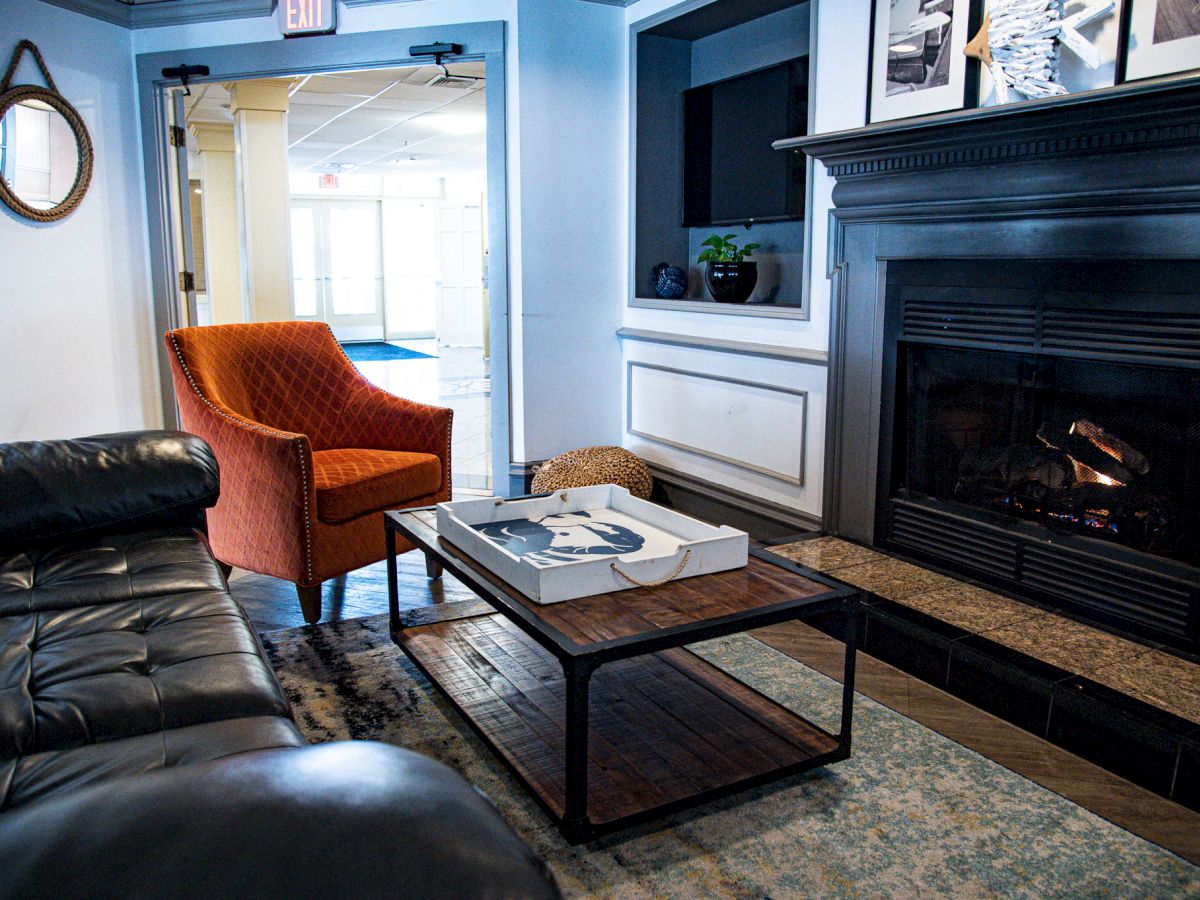 A cozy living room with a leather couch, orange chair, fireplace, and coffee table. The room is decorated with a mirror and pictures.