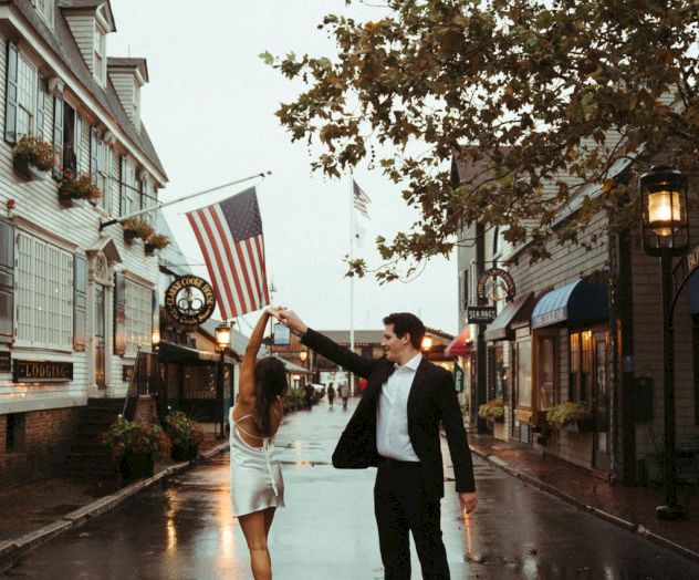 A couple dances on a wet street lined with charming buildings and American flags, creating a romantic atmosphere.