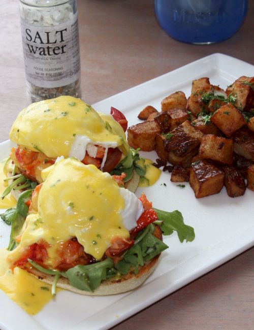 The image shows eggs Benedict with hollandaise sauce on a plate alongside roasted potatoes, with a salt grinder nearby.