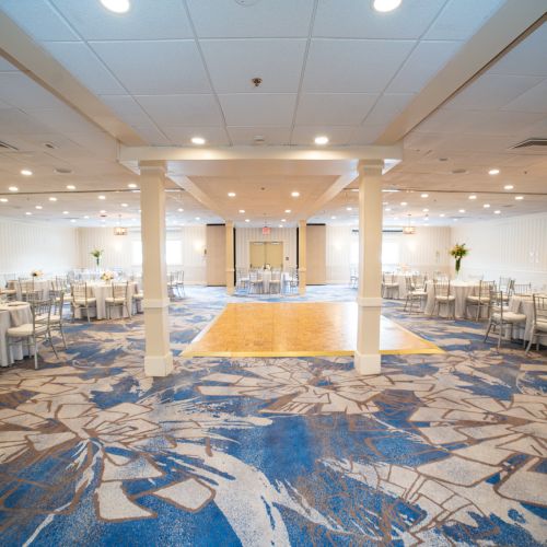 A spacious banquet hall with a dance floor, set tables, chairs, and elegant floral centerpieces is featured in the image.