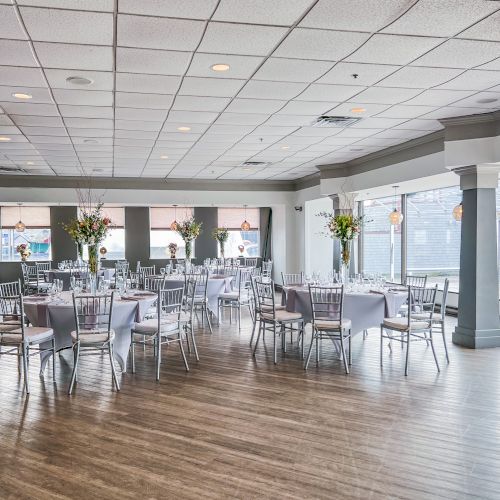 The image shows a banquet hall with round tables set for an event. The tables have white tablecloths and flower centerpieces.