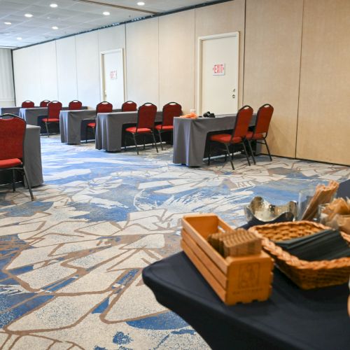 The image shows a conference room with tables and red chairs. In the foreground, there's a table with refreshments and snacks displayed.