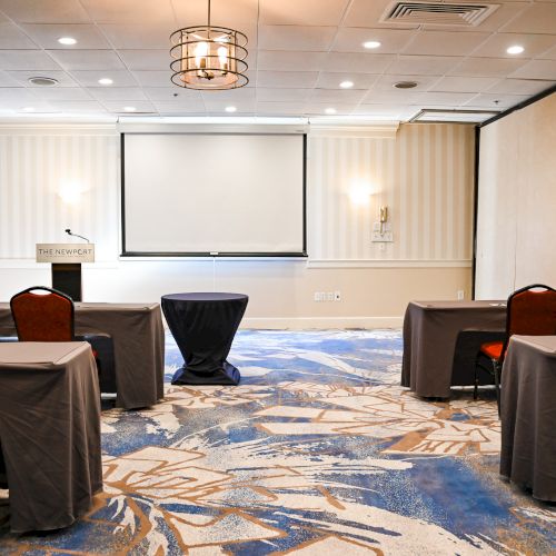 The image shows a conference room with tables, chairs, a projector screen, and a podium, set up for a meeting or presentation.