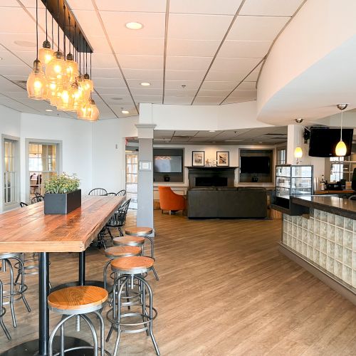 The image shows a modern cafe interior with wooden tables, stools, hanging lights, and a coffee counter.