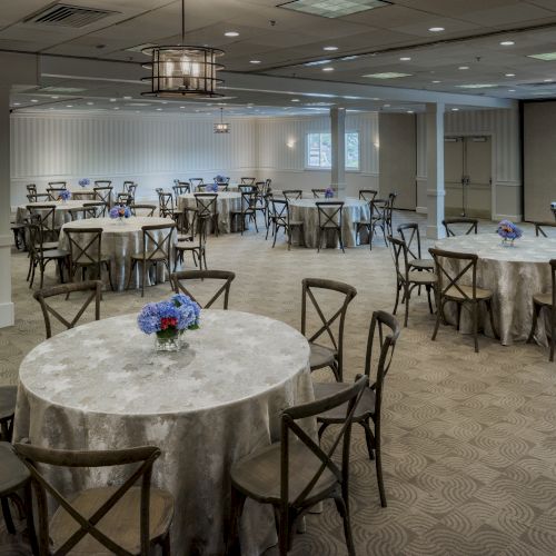 An event hall with round tables covered in tablecloths, each with a floral centerpiece, and neatly arranged chairs around them.