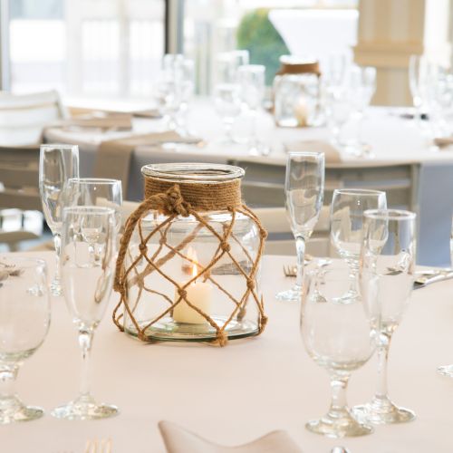 A table set with glassware and a decorative jar centerpiece wrapped in rope, creating an elegant dining arrangement.