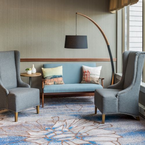 The image shows a seating area with two armchairs, a small couch, a side table with tea sets, and a large lamp, on a patterned carpet.