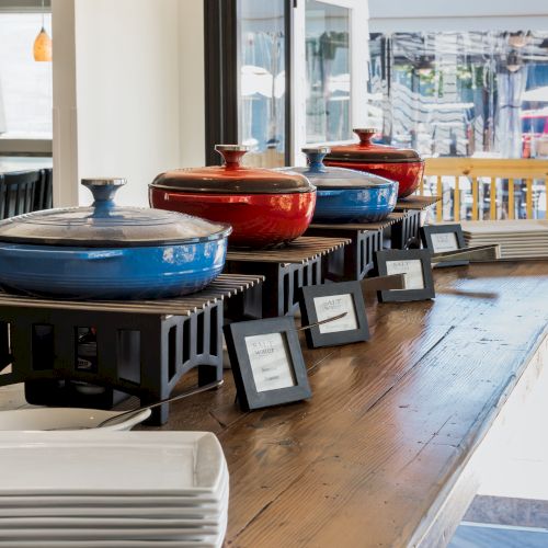 The image shows a buffet setup with three covered pots on stands, plates beside them, and small signs on a wooden table.