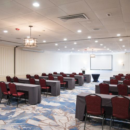 This image shows a conference room with arranged tables and chairs, a projector screen at the front, and a patterned carpet.