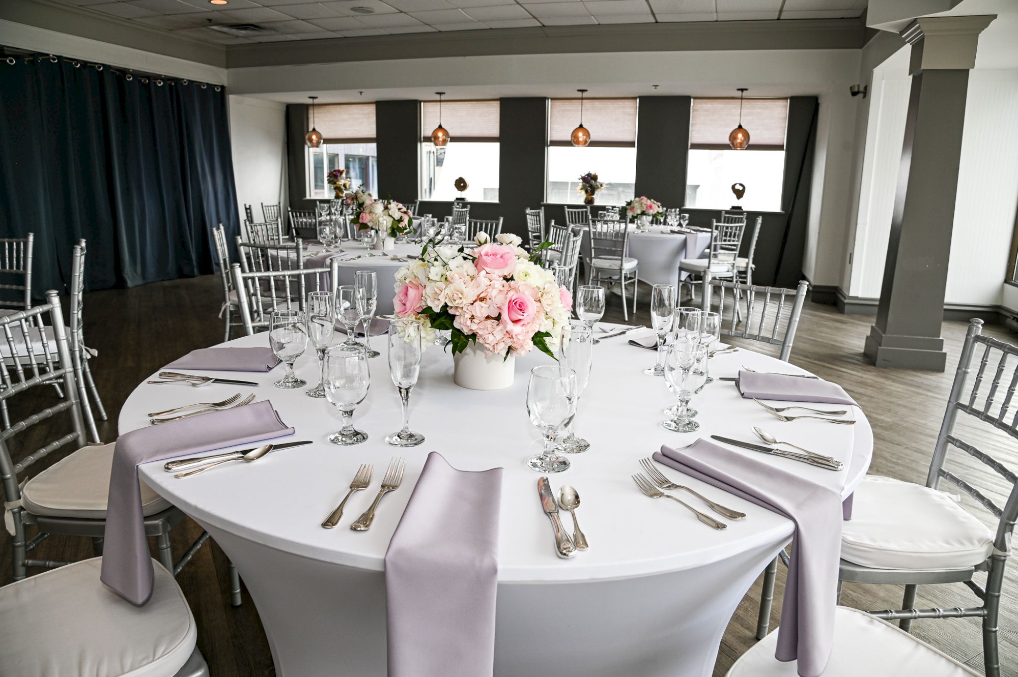 A beautifully set dining table with floral centerpiece and elegant place settings in a bright, modern room with large windows.